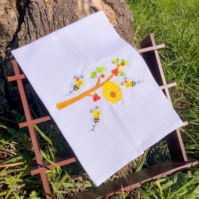 Toalha branca bordada com tema de abelhas sobre estrutura de madeira ao ar livre