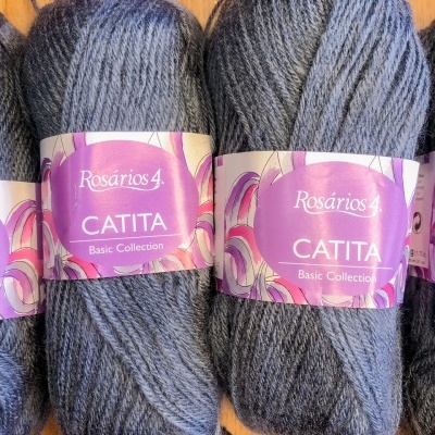 Novelos de lã cinzenta escura Rosários 4 coleção Catita com rótulo roxo sobre madeira clara