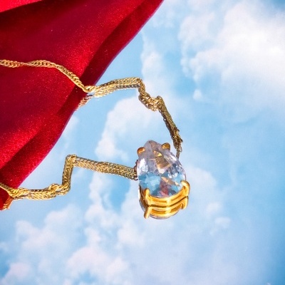 Colar com pendente de pedra azul sobre fundo refletindo céu azul e nuvens