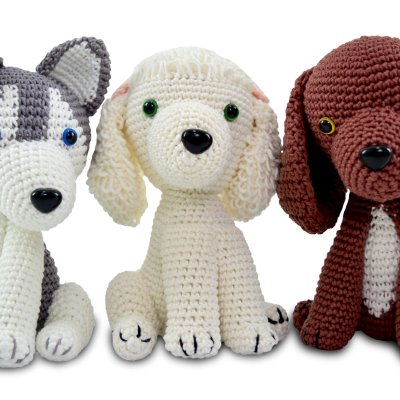 Três cães de peluche feitos em crochet com cores cinzento, creme e castanho