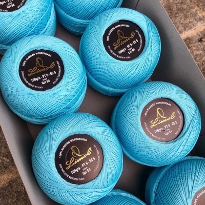 Oito novelos de linha azul claro com etiquetas pretas numa caixa cinzenta sobre pedra