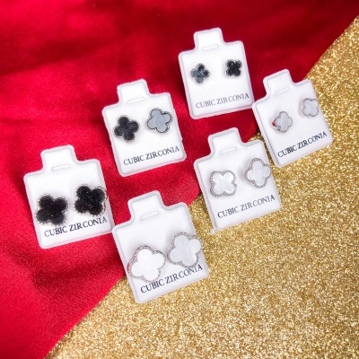 Seis pares de brincos de zircónia cúbica em suportes brancos sobre fundo vermelho e dourado glitter