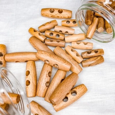 Botões de madeira cilíndricos com furos sobre tecido branco e dentro de frascos de vidro