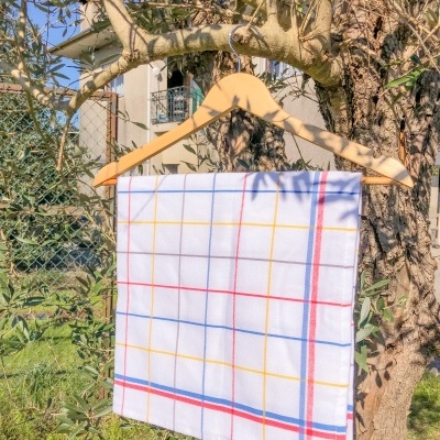 Pano de cozinha branco com linhas de grelha coloridas pendurado em cabide de madeira numa árvore ao ar livre