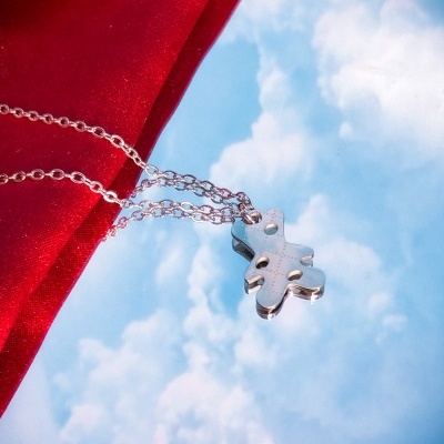 Colar prateado com pendente em forma de cruz contra céu azul com nuvens e tecido vermelho