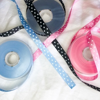 Rolos de fita de cetim azul, preta e rosa com bolinhas brancas sobre tecido branco