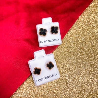 Dois pares de brincos florais pretos e dourados em suportes brancos com texto CUBIC ZIRCONIA, sobre fundo vermelho e dourado