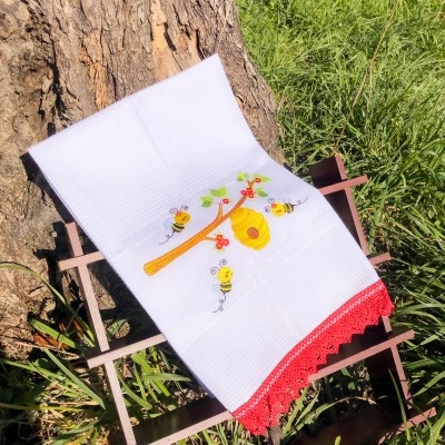 Toalha bordada branca com padrão de abelhas e renda vermelha ao ar livre