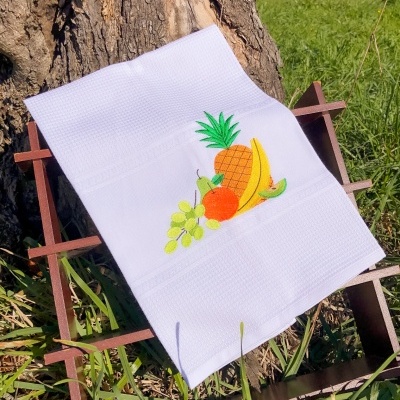 Toalha branca com bordado de frutas pendurada numa estrutura de madeira ao ar livre