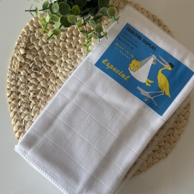 Fralda dupla branca com etiqueta azul e ilustração sobre esteira de fibras naturais