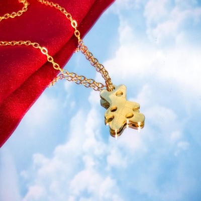 Colar dourado com pendente em forma de folha sobre fundo vermelho e espelho refletindo céu