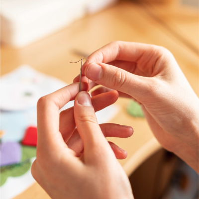 Duas mãos a manusear uma agulha de costura com linha preta