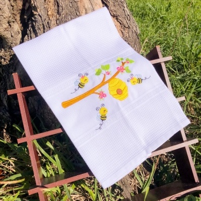 Pano de prato branco com bordado de abelhas e favo de mel ao ar livre
