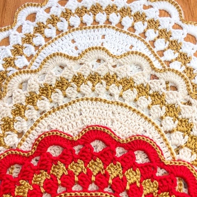 Toalhas de crochê redondas com bordas onduladas coloridas em branco, bege, dourado e vermelho em madeira clara.
