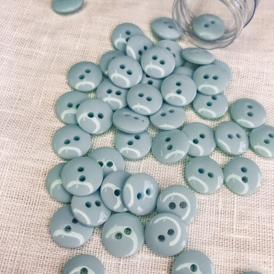 Botões redondos verdes em tecido bege ao lado de recipiente plástico.