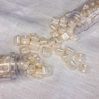 Contas de cor pérola espalhadas sobre tecido branco com duas embalagens plásticas abertas