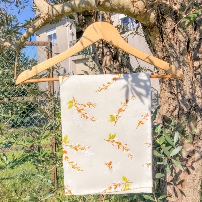 Toalha bege com padrão floral pendurada em cabide de madeira numa oliveira