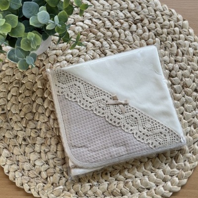 Toalha branca com renda e laço sobre base trançada com planta verde