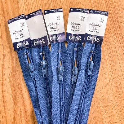 Cinco fechos éclair azuis com etiquetas sobre uma superfície de madeira clara