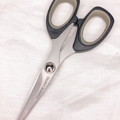 Tesoura com lâminas revestidas a titânio e cabos pretos e bege sobre tecido branco