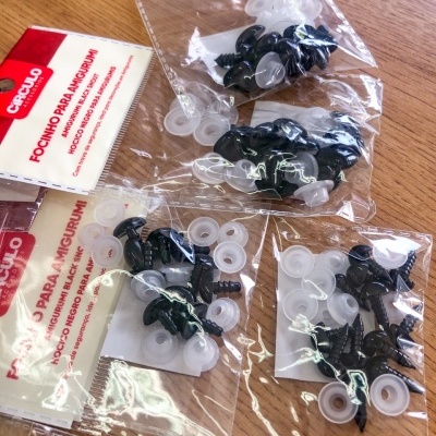 Embalagens de olhos de segurança para amigurumi sobre mesa de madeira