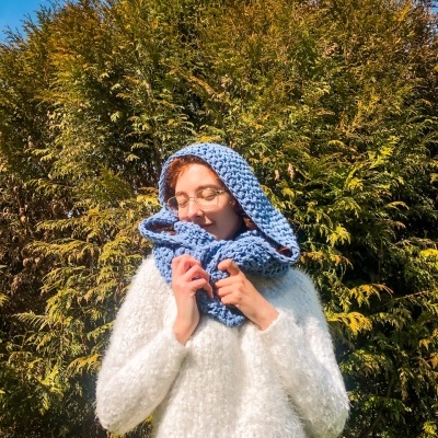 Mulher com suéter branco felpudo e cachecol de malha azul claro ao ar livre em dia de sol