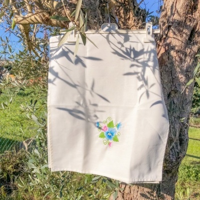 pano de cozinha branco com bordado de flores coloridas pendurado numa árvore