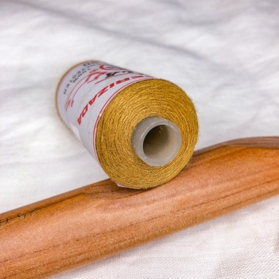 Rolo de linha dourada e cabide de madeira sobre tecido branco