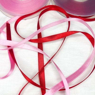 Rolos de fita de cetim rosa e roxo com fitas rosa e vermelha desenroladas sobre fundo branco