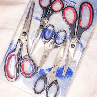 Conjunto de cinco tesouras com cabos preto e vermelho numa embalagem de plástico transparente