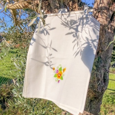 Toalha branca bordada pendurada em árvore com sombra e céu azul