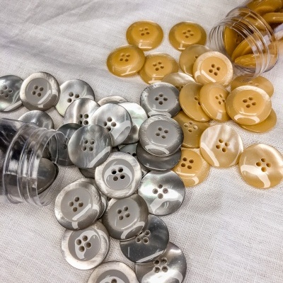 Botões redondos bege e cinza marmoreado com quatro furos em tecido branco