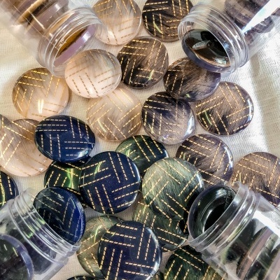 Botões redondos transparentes com padrão listrado dourado em cores variadas em frascos e sobre tecido branco