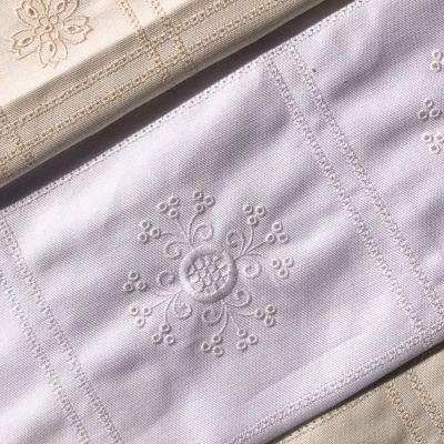 Toalhas bordadas em creme e branco com padrões florais e geométricos