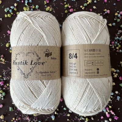 Novelos de fio de algodão cru Rustik Love com etiquetas castanhas sobre fundo escuro com flores coloridas