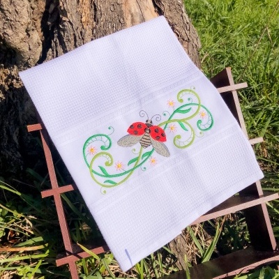 Toalha branca com bordado de joaninha e folhas verdes