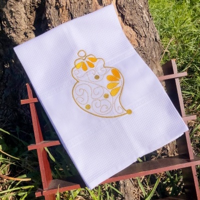 Toalha branca com bordado amarelo em suporte de madeira junto a uma árvore