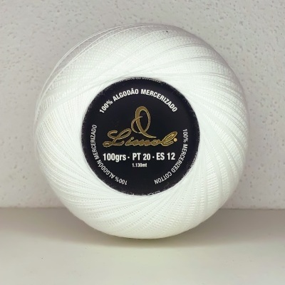 Novelo de linha branca com rótulo preto e letras douradas sobre fundo branco texturado