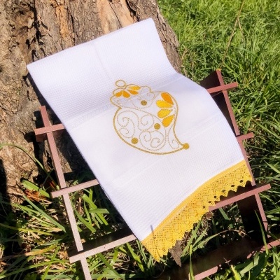 Toalha branca bordada com sino amarelo e renda amarela sobre suporte de madeira ao ar livre