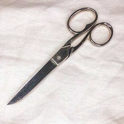 Tesoura metálica prateada sobre tecido branco