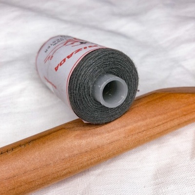 Rolo de linha cinzenta com etiqueta vermelha sobre tecido branco e madeira clara