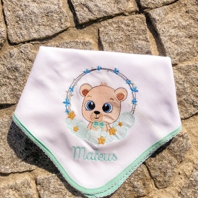 Babete branco com bordado de urso e nome Mateus em fundo de pedras