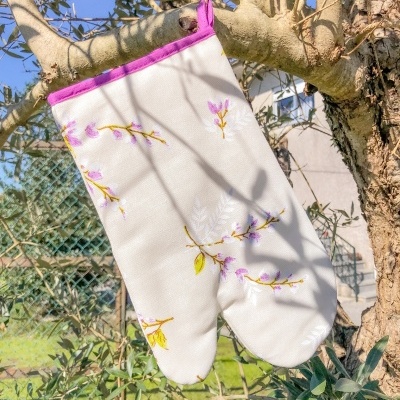 Luva de forno bordada branca com acabamento rosa pendurada numa árvore