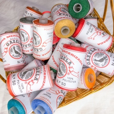 Carretéis de linha colorida 100% poliéster com rótulos brancos numa cesta dourada