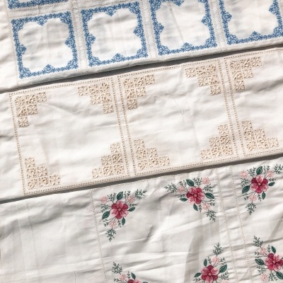 Panorama de três panos de mesa bordados com padrões em azul, bege e flores vermelhas e verdes.