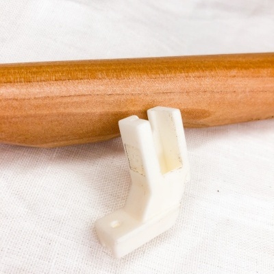 Peça plástica branca angular junto a superfície cilíndrica de madeira clara sobre tecido branco