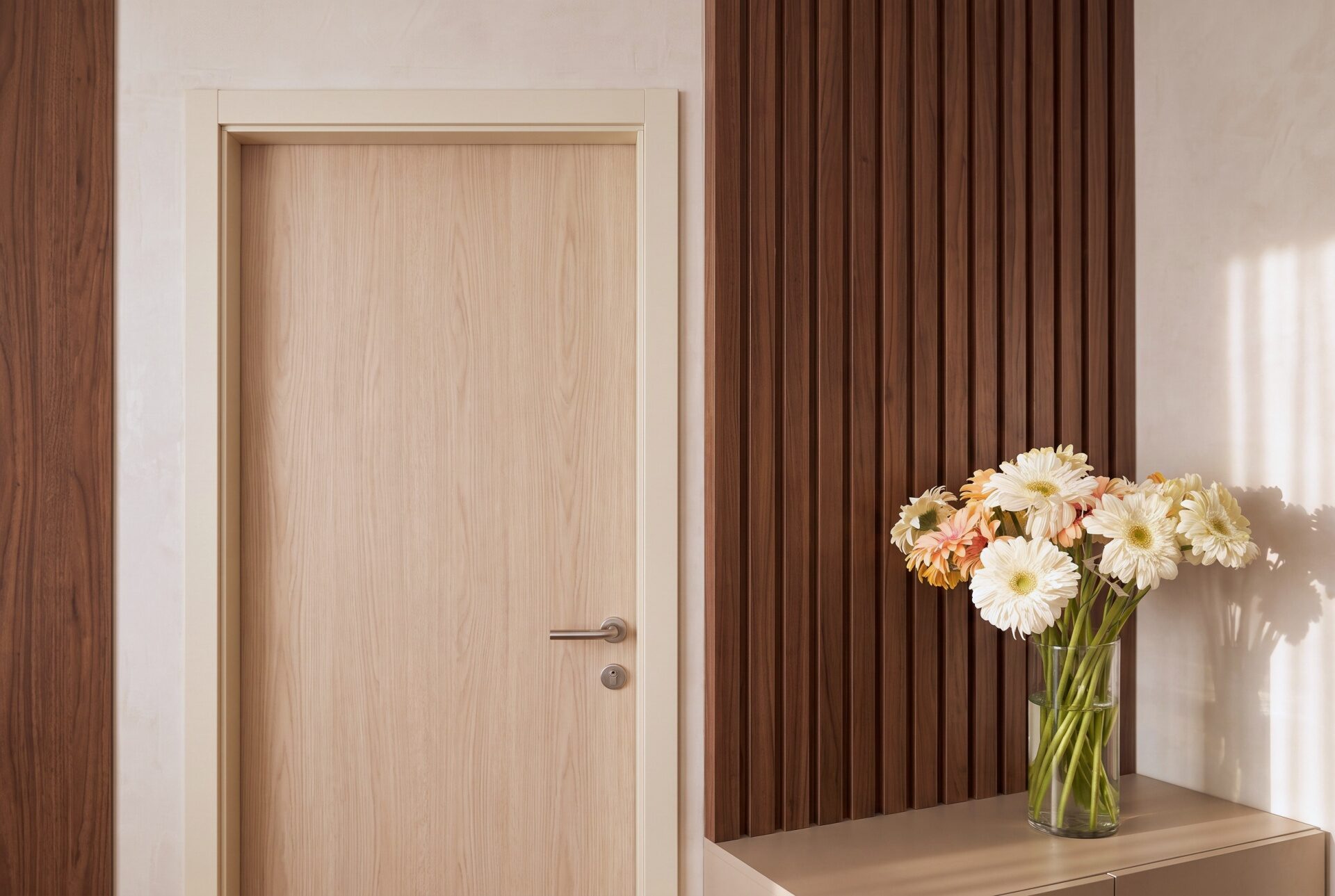 Entrada interior da Riarte Clinic, com ripado de nogueira e flores sobre o m&oacute;vel