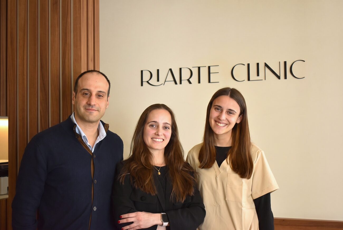 Três profissionais da Riarte Clinic diante do letreiro de parede