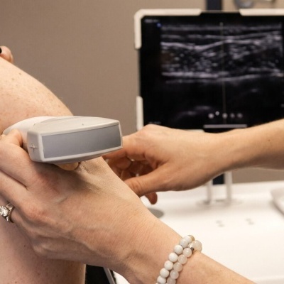 Ultrassom médico a ser realizado no braço de uma pessoa com pele clara e manchas.