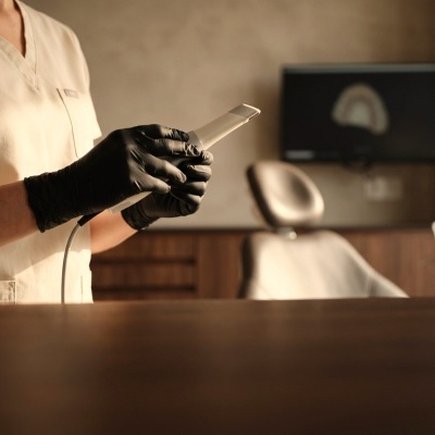 Profissional de saúde com dispositivo branco e luvas pretas junto a cadeira de clínica